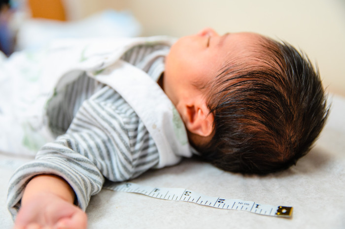 baby lying down on his back with a measuring tape next to him