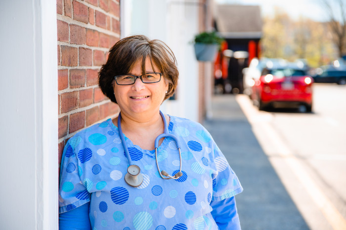 a woman wearing a stethoscope leaning against a brick wall outside